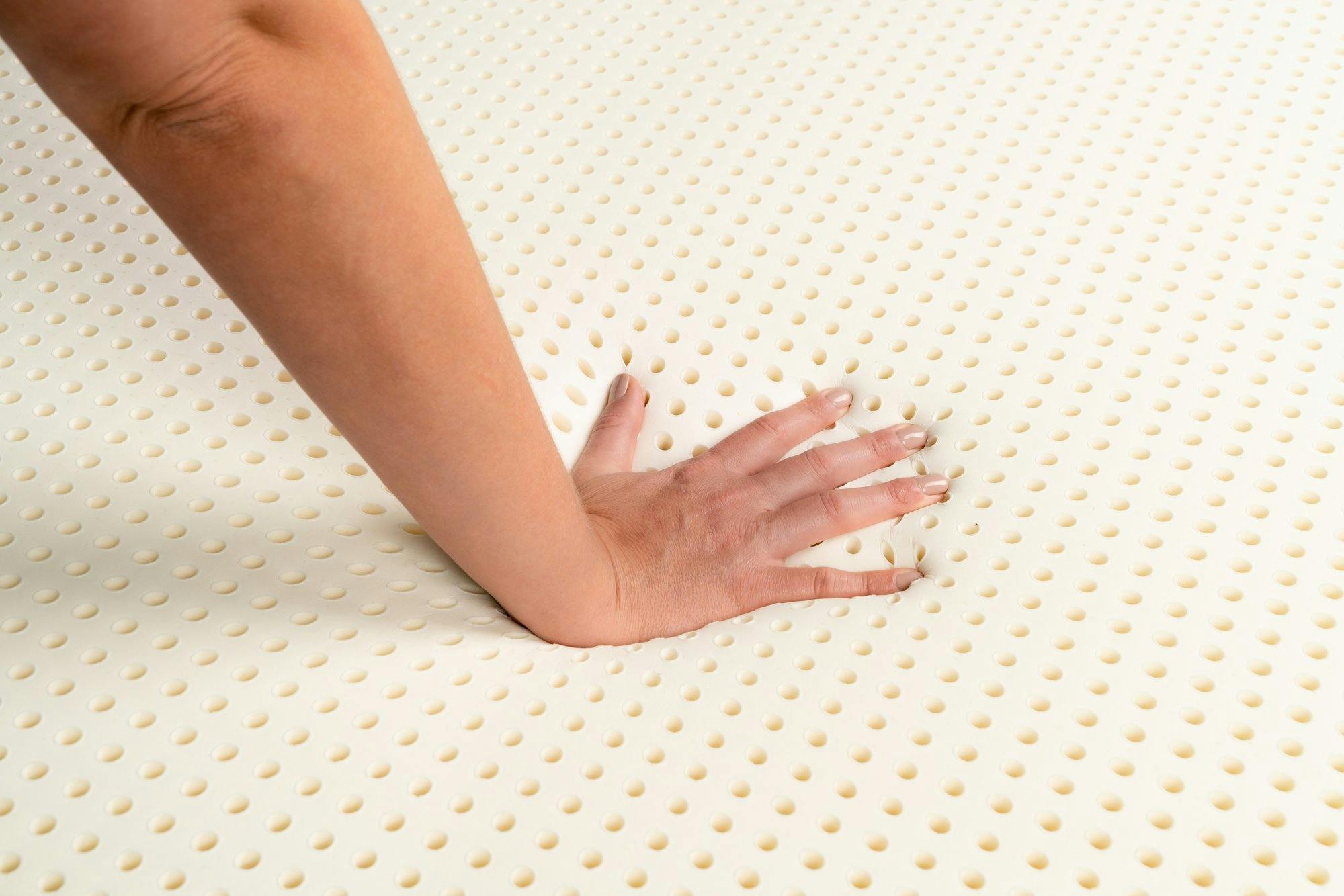 Hand pushing down on a latex foam mattress